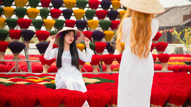 游客在越南广富桥村晾晒的香签旁拍照 (来源:新华社)